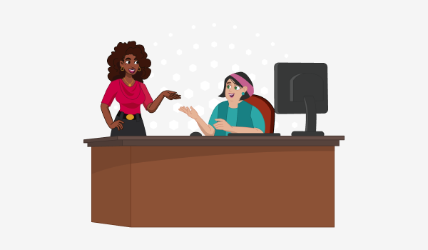 A woman sitting at a desk talks happily with a woman standing next to her.