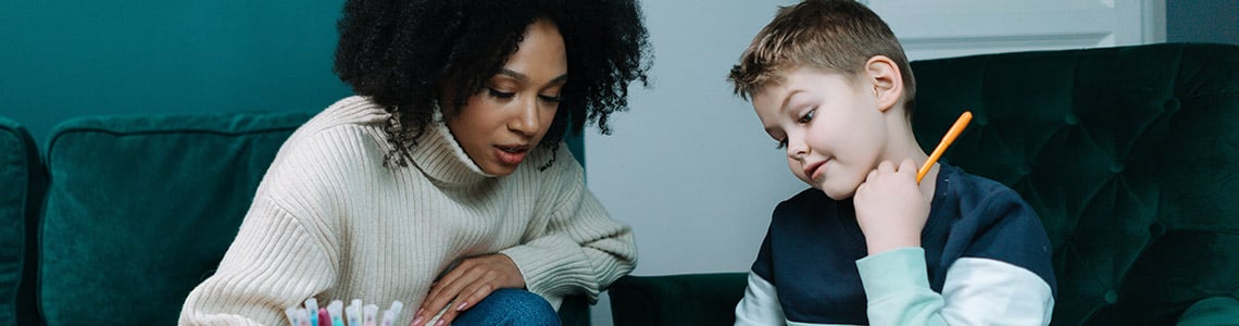 A teacher tutoring a young boy who is holding a pencil