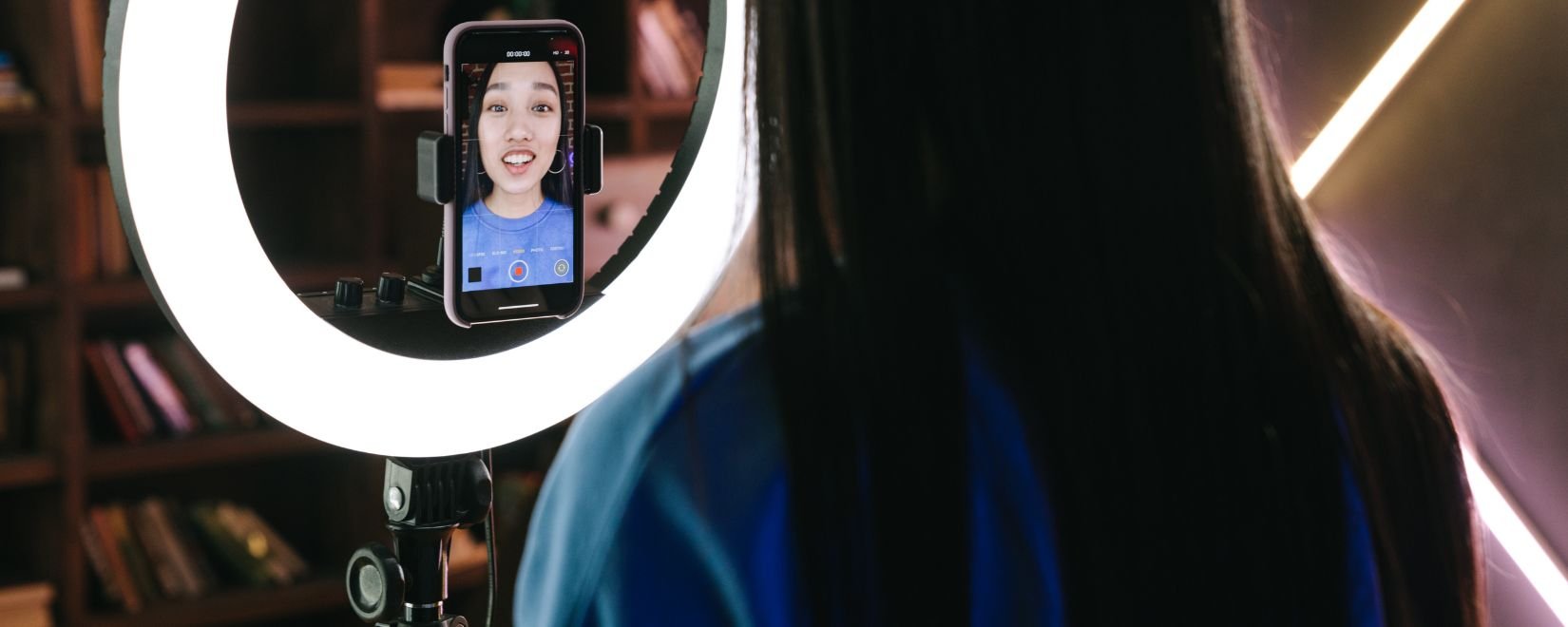 A woman in front of a ring light, recording a video on a smartphone