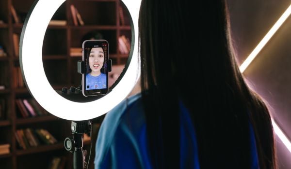 A woman in front of a ring light, filming herself on a smartphone