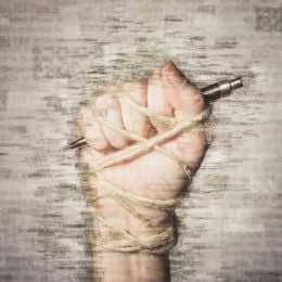 A clenched fist wrapped in twine holding a pen against a background of words