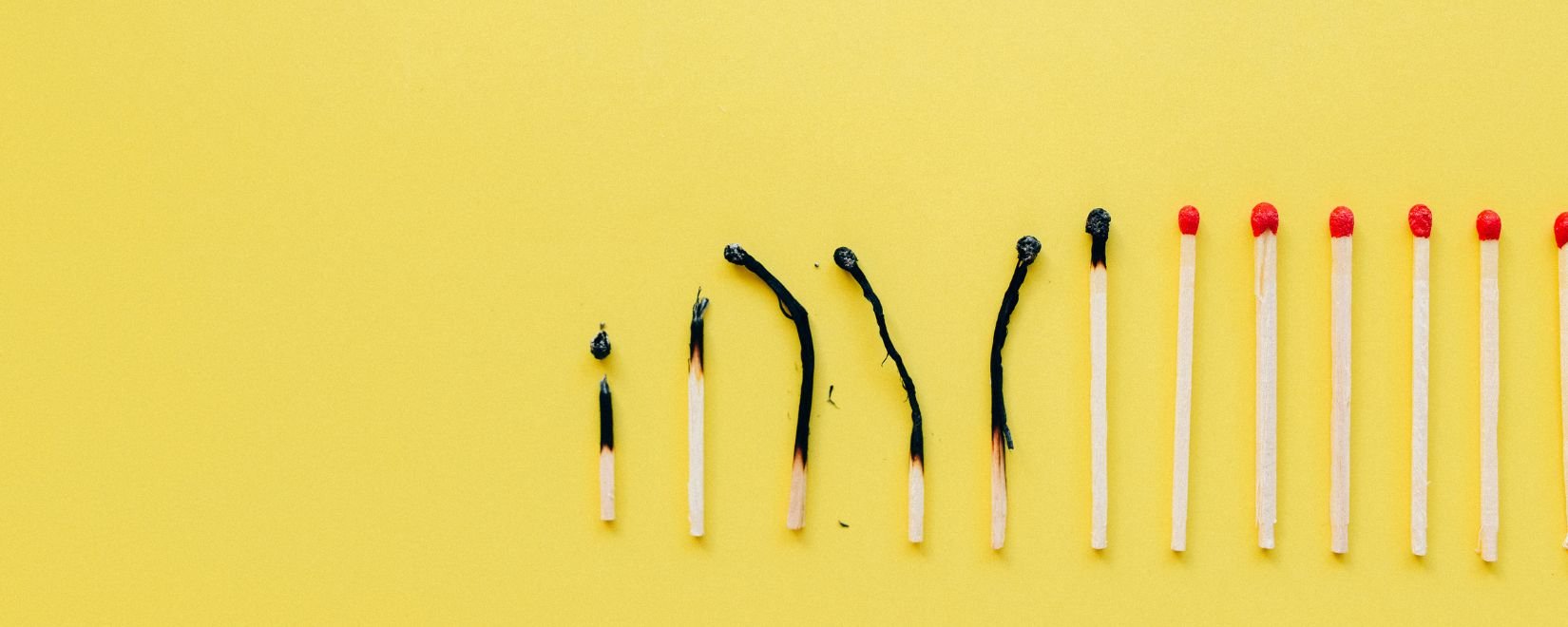A line of matches, some burnt and some unburnt on a yellow background.