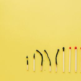 A line of matches, some burnt, some unburnt, on a yellow background 