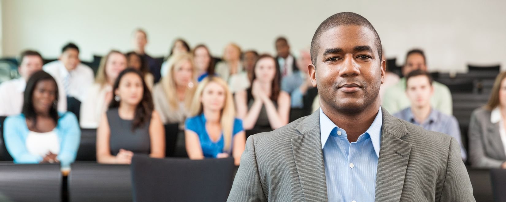An African-American male teacher standing in front of a group of college students 