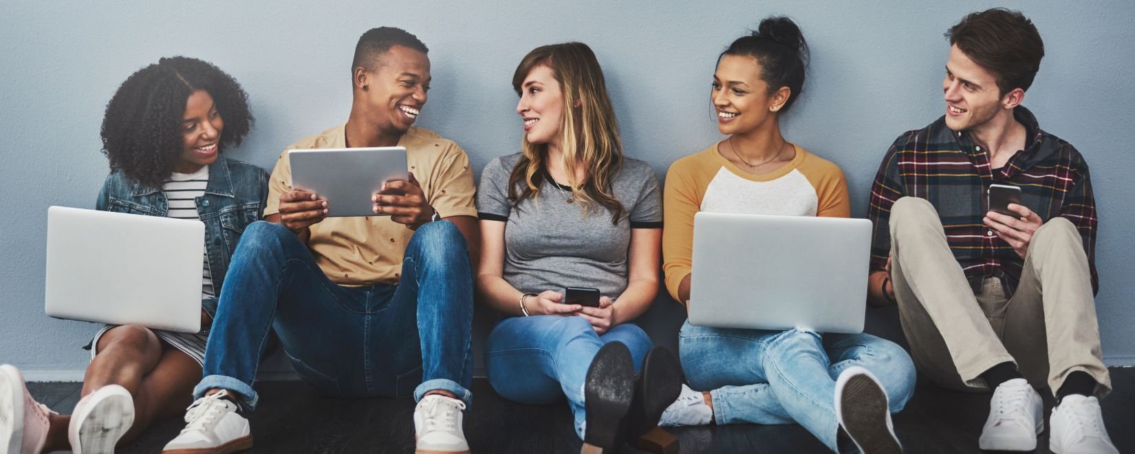 A group of young people sitting in a row, holding laptops and smiling