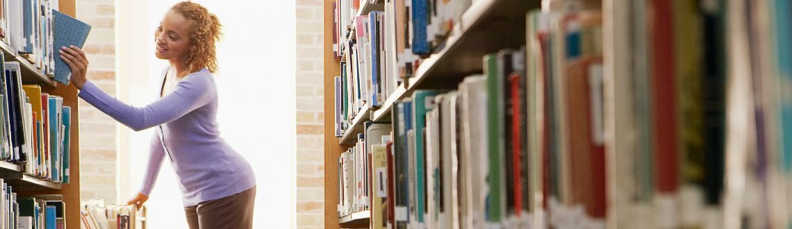 Woman pushing a book cart and placing a book on a shelf in a library