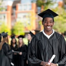 An African-American male student in a cap and gown holding a diploma