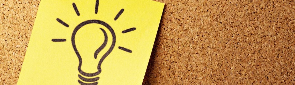 A sticky note with a lightbulb on it posted on a cork board