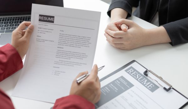 Close up of hands holding a pen and resume. Someone else's hands are clasped across the desk