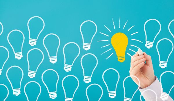 A bright blue background with a hand drawing white and yellow lightbulbs