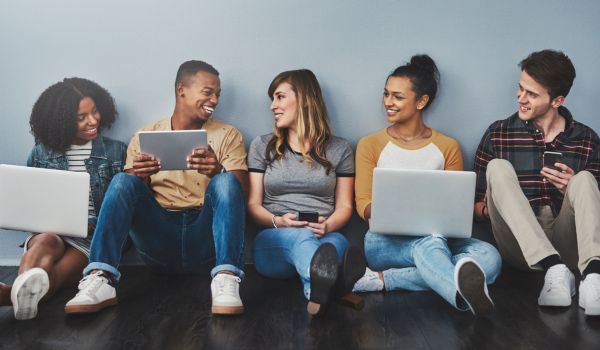 A group of young people sitting in a line, holding laptops and smiling